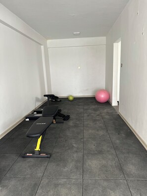 Une salle de sport équipée de matériel d’exercice, d’un banc, d’un tapis vert et d’un ballon d’exercice rose, ainsi que d’un luminaire fixé au mur.