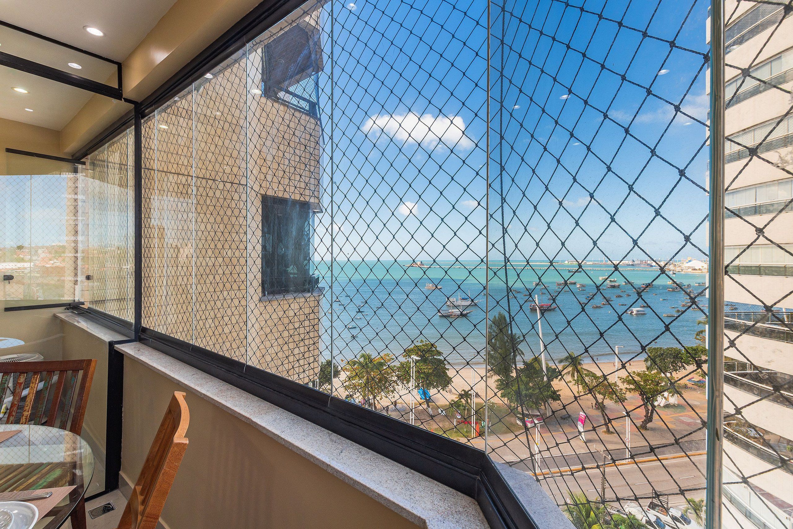 A hotel room with a view of the sea through a chain-link fence.