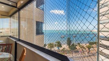 A hotel room with a view of the sea through a chain-link fence.