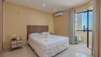 A hotel room with a bed, bedside table, lamp, and an air conditioning unit.