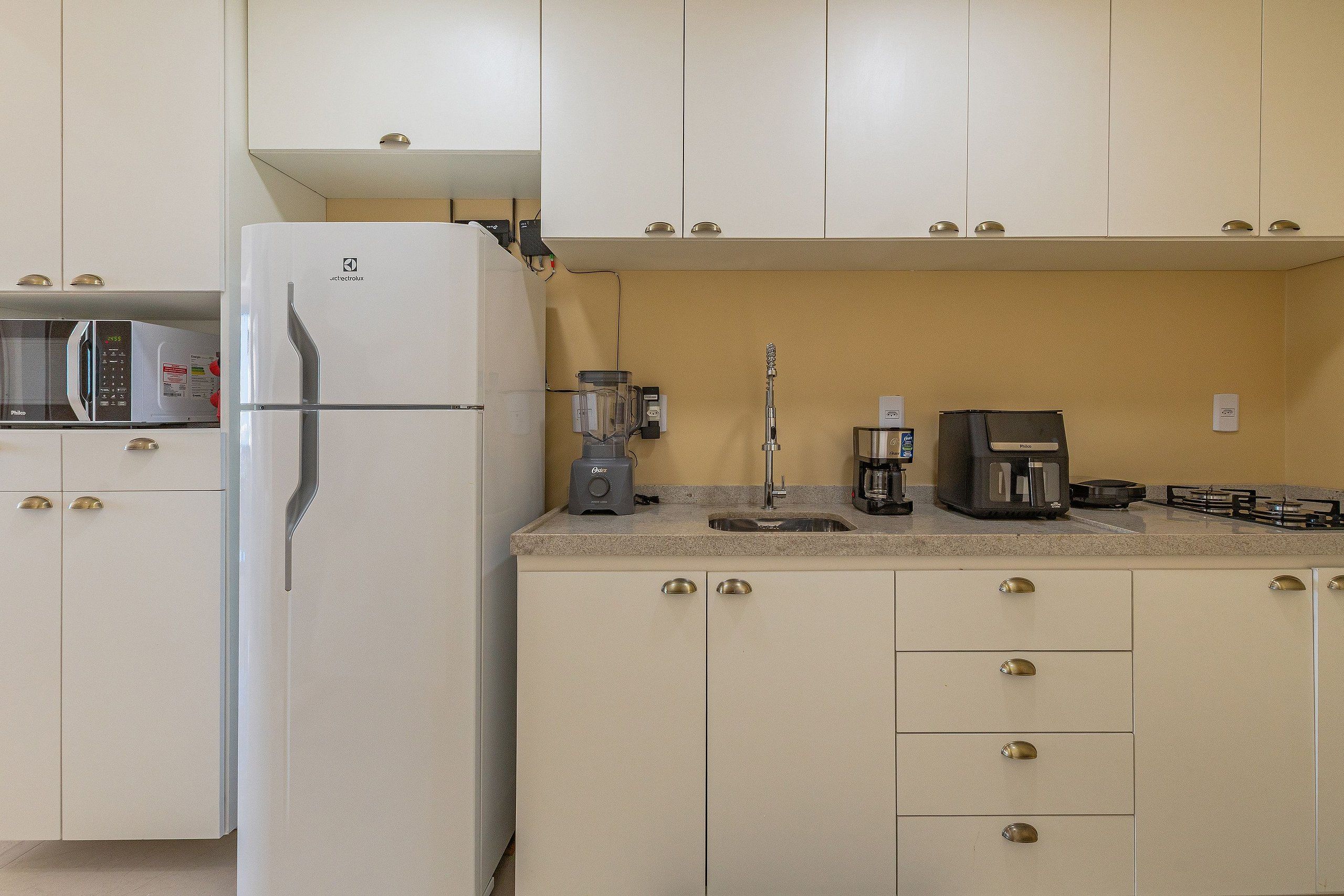 Cozinha compacta com geladeira branca, cafeteira, liquidificador e jarra para café na bancada.