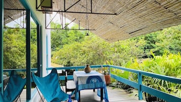 A covered outdoor area with a table and chairs, surrounded by lush greenery.