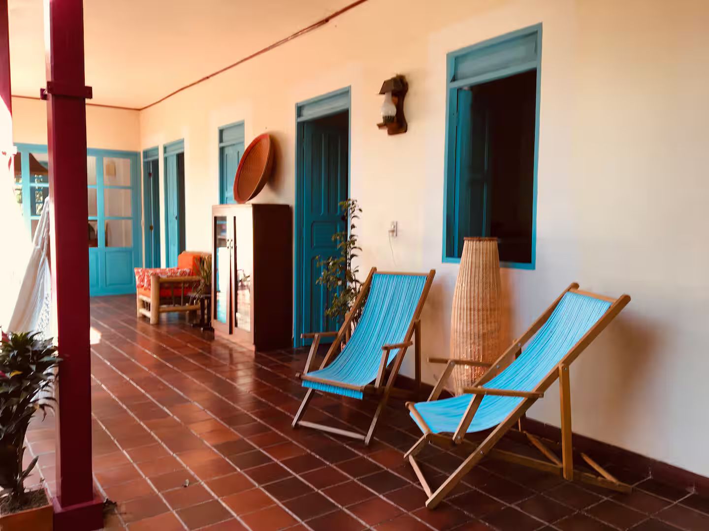 A room with a tiled floor, a sofa, two blue hammocks, a lamp, and a door with a blue frame.