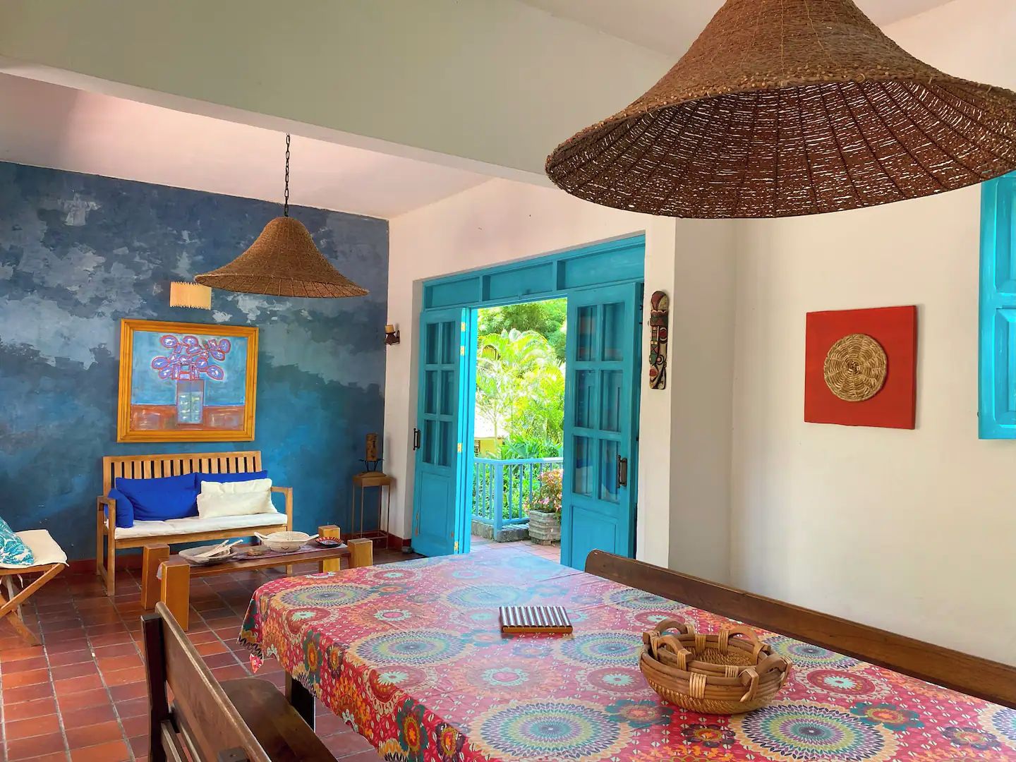 A room with a bed, a table, and a chair. There is a door leading to an outdoor area.