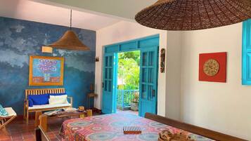 A room with a bed, a table, and a chair. There is a door leading to an outdoor area.