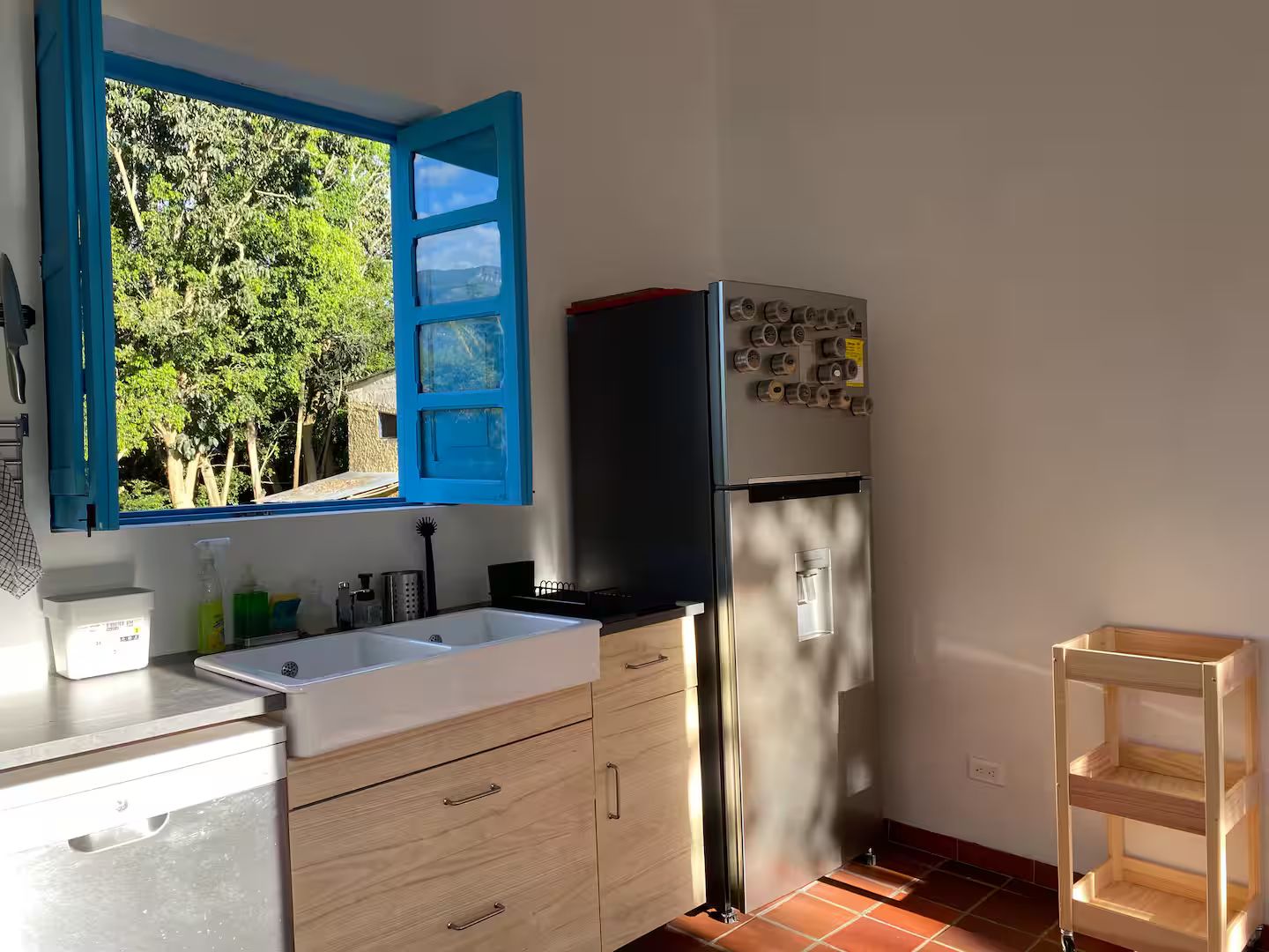 A kitchen with a window, a refrigerator, and a wooden shelf.