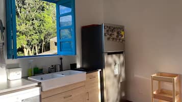 A kitchen with a window, a refrigerator, and a wooden shelf.
