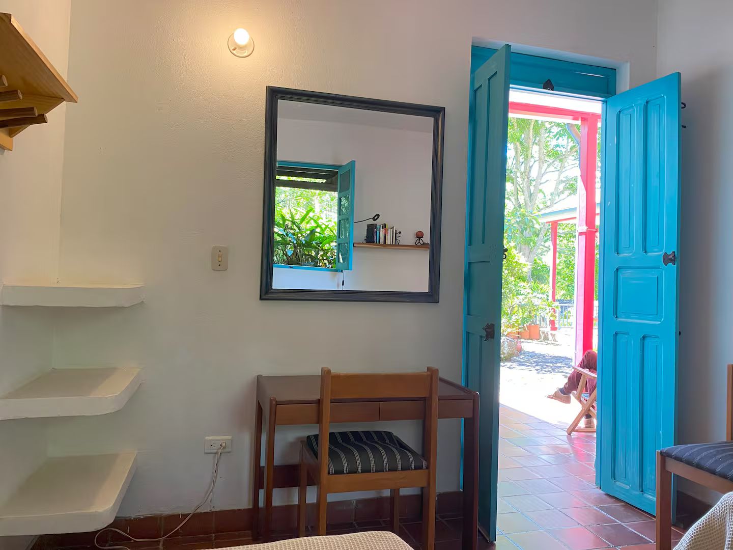 A room with a bunk bed, a mirror, a blue door, and a view of the outside.