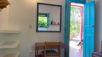 A room with a bunk bed, a mirror, a blue door, and a view of the outside.