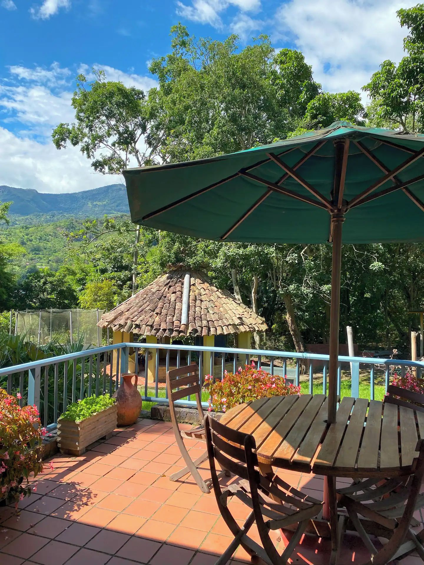 Une terrasse avec une table et des chaises, une structure à toit de chaume et une vue sur un paysage montagneux.