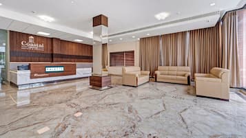 Ein Empfangsbereich mit einer Rezeption, einer Sitzecke mit Sofas und Sesseln sowie einem großen Fenster mit Vorhängen.