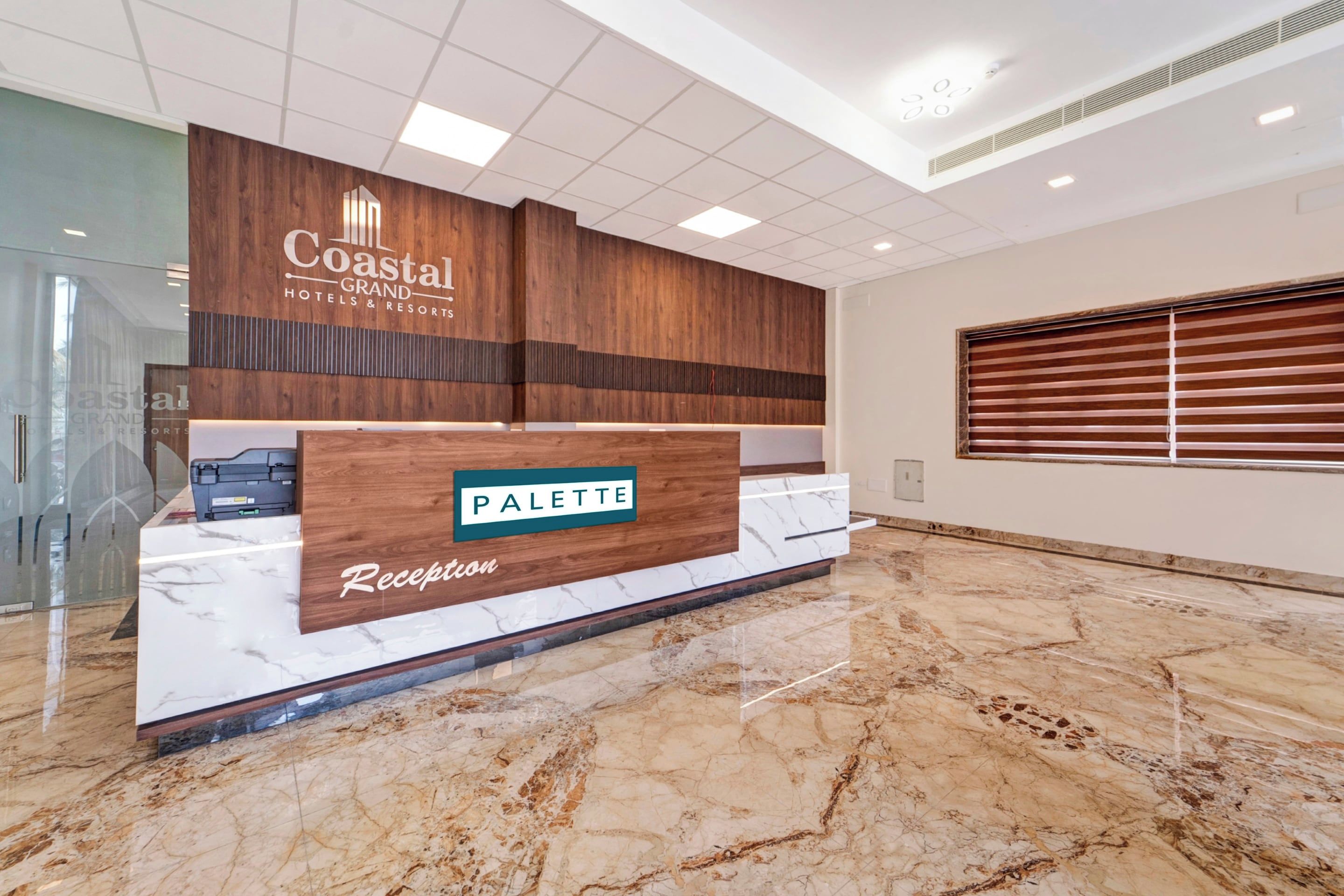 A reception desk with a wooden panel design, a marble countertop, and a sign that reads 'Coastal Grand Hotels & Resorts.'