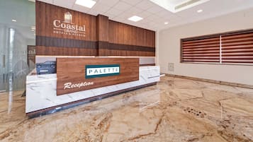 A reception desk with a wooden panel design, a marble countertop, and a sign that reads 'Coastal Grand Hotels & Resorts.'