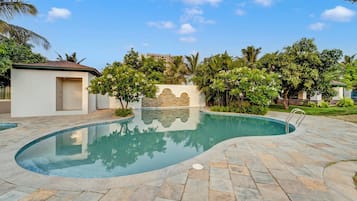 A swimming pool with a curved design, surrounded by a stone patio and lush greenery.