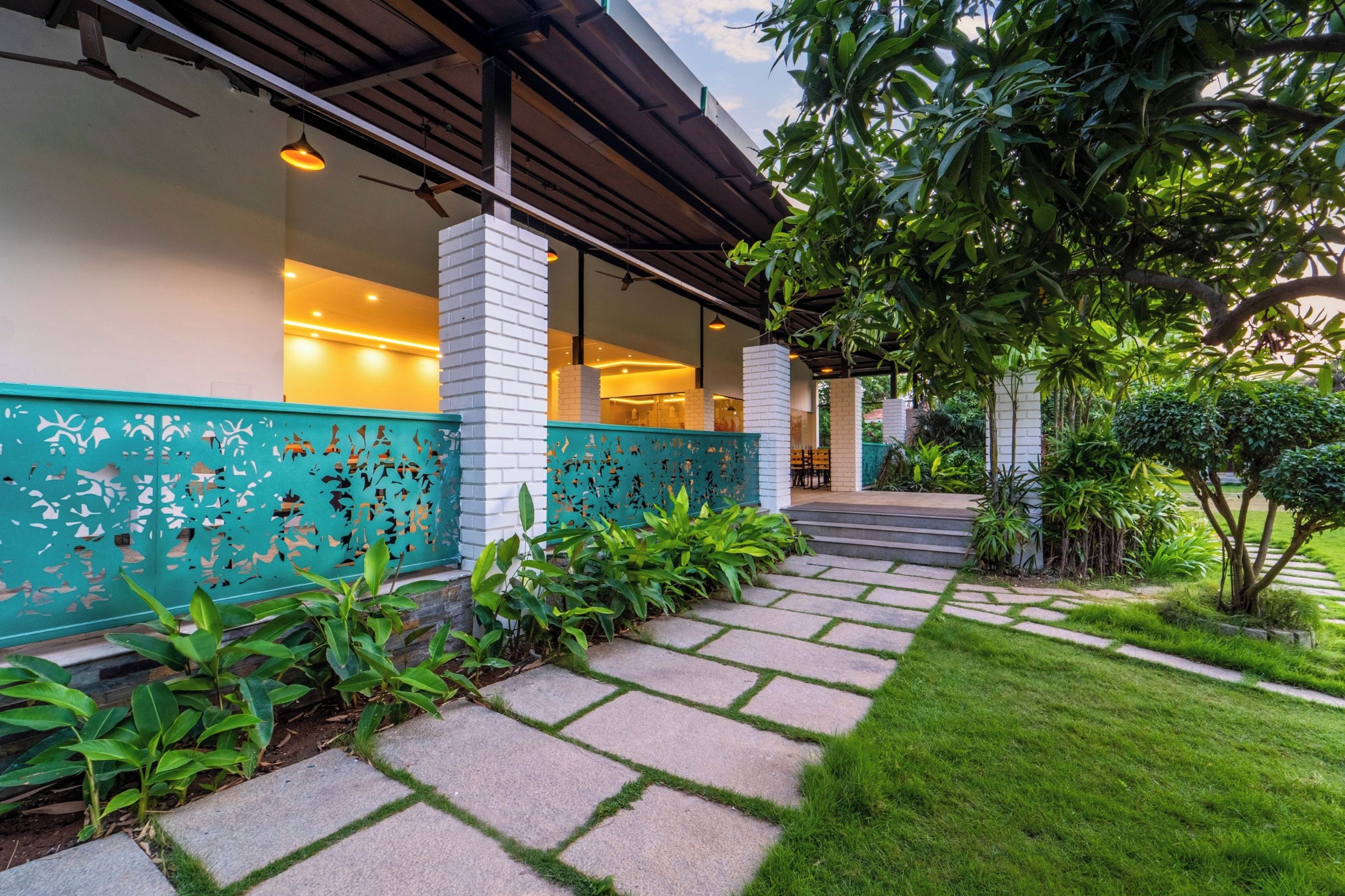 A modern building with a covered walkway, a brick column, and a green decorative fence.