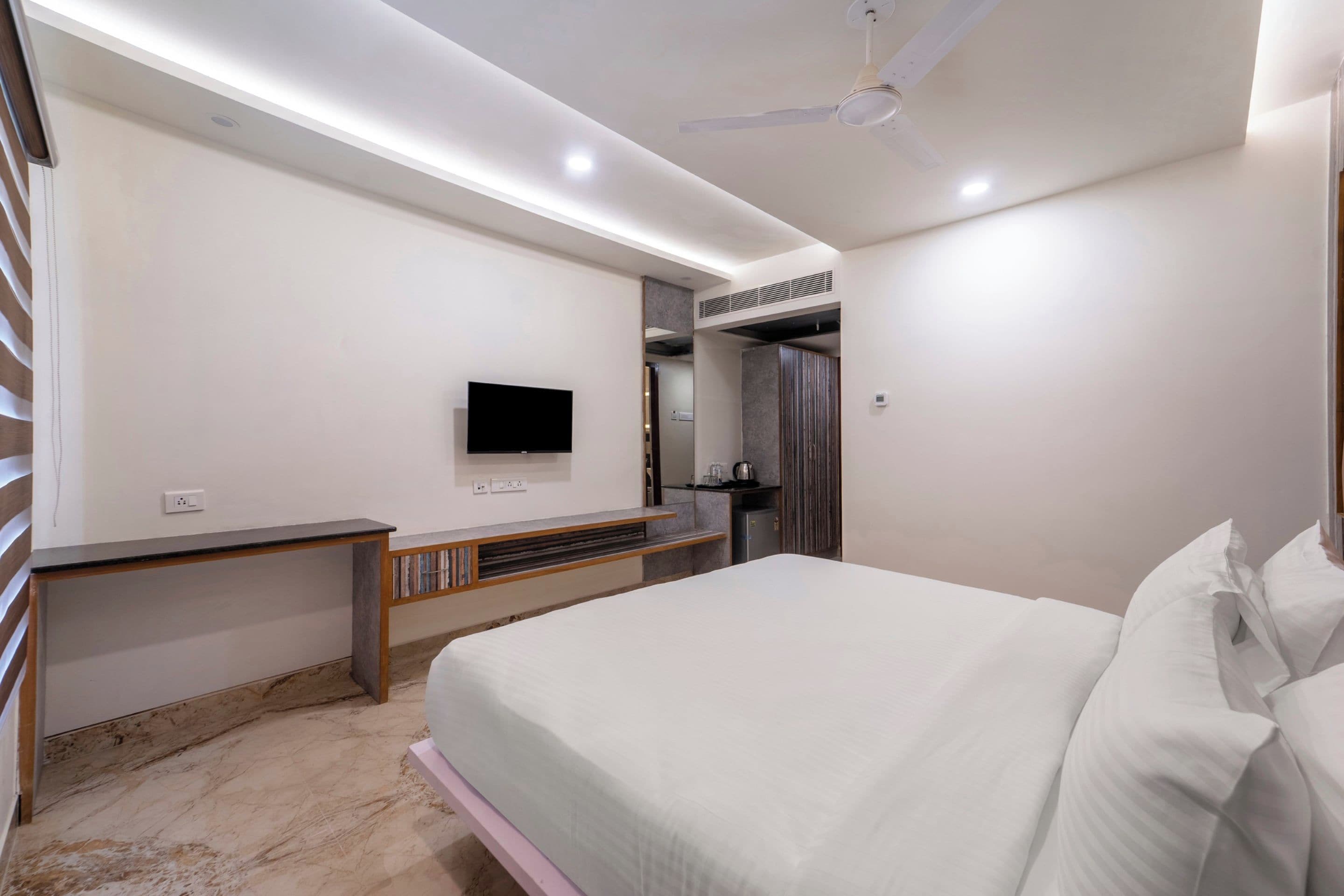 Un dormitorio moderno con una cama, un televisor de pantalla plana, un ventilador de techo e integrado un banco.