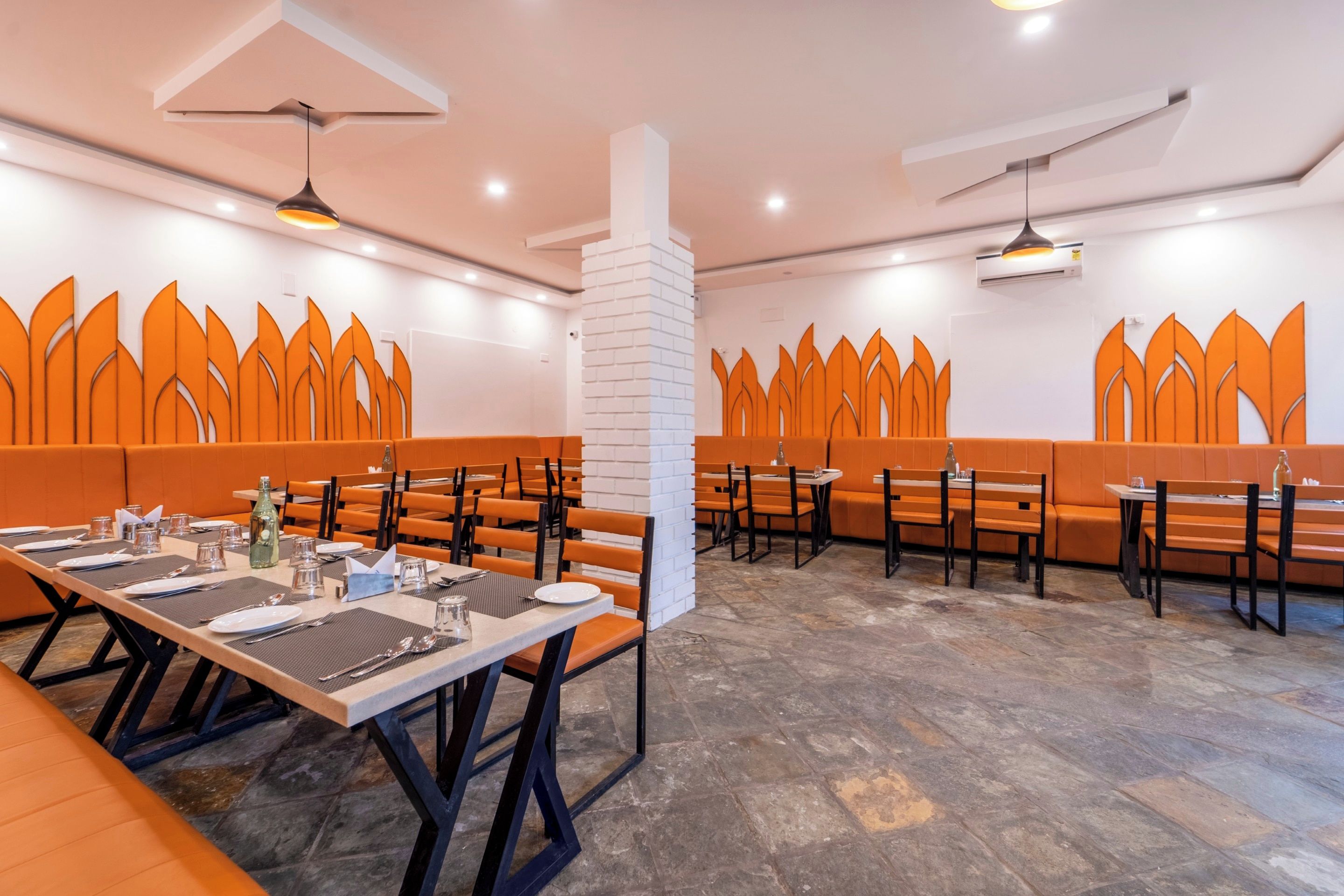 Ein Restaurant mit orangefarbenen Sitzbänken und Tischen, weißen Säulen und einem Steinfußboden.