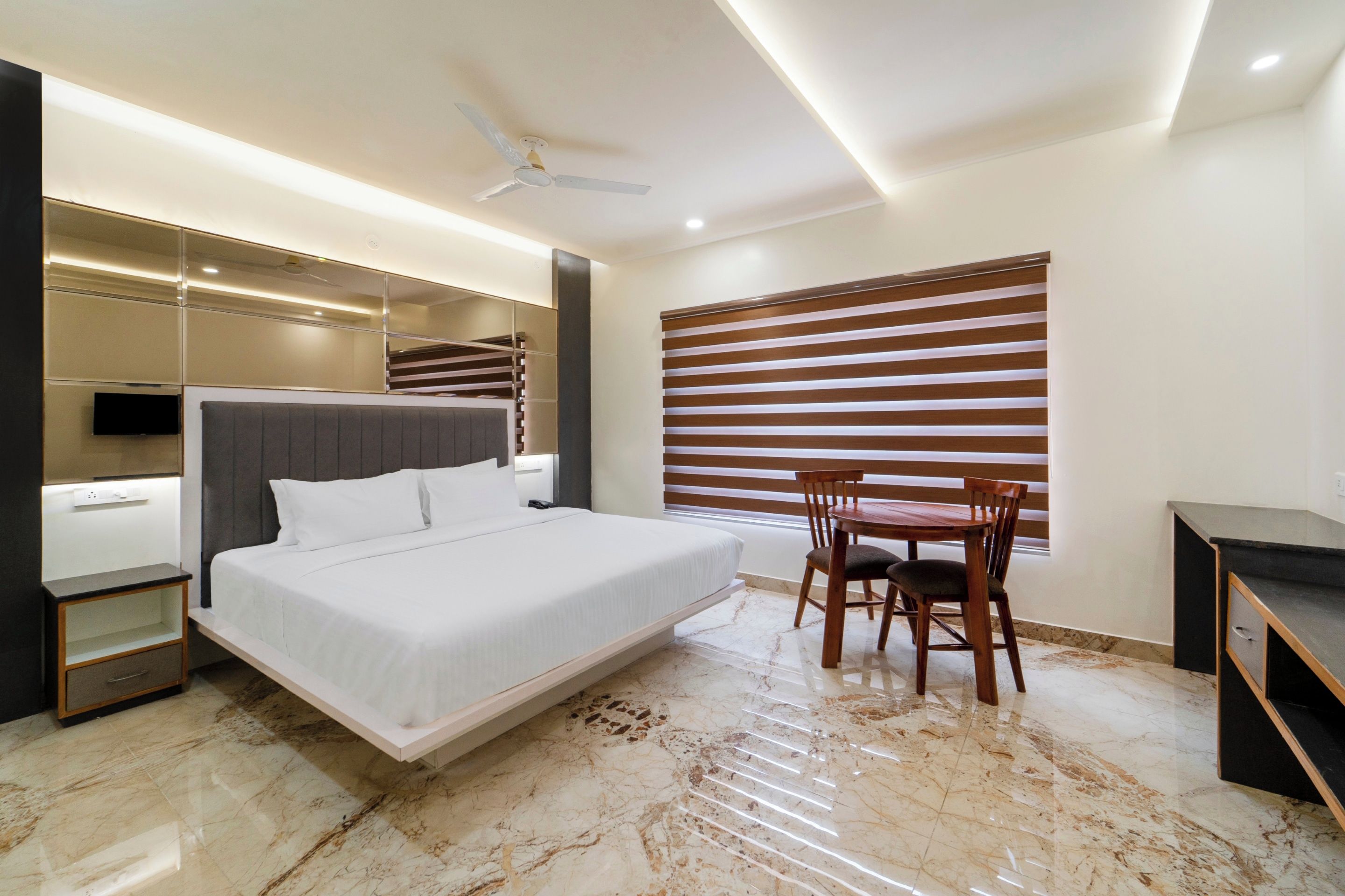 A modern hotel room with a bed, a desk, a chair, a TV, and a window with blinds.