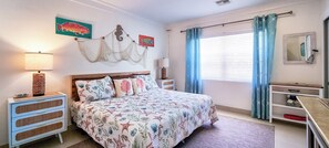 A bedroom with a bed, bedside tables, a dresser, a window with curtains, and wall decorations. - Hog Plum 3-bedroom 2 minute walk to the beach with Kayak and paddle board (Spanish Wells)