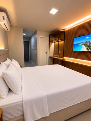 A hotel room with a bed, a TV mounted on a wooden panel wall, and a hallway leading to another room. - Estúdio aconchegante de 1 quarto com ar-condicionado na maravilhosa Maceió. (Maceió)