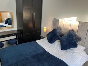 A bedroom with a bed, a desk, a wardrobe, and a nightstand with a lamp. - House Sleeps 4 - Private Garden - Bbq (York)