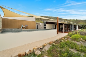 A modern house with a swimming pool, outdoor seating, and a view of a hilly landscape. - Elysian Allure Oceanfront Paradise with Pool and Spa (Normanville)