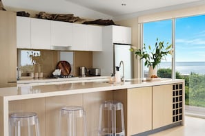 A modern kitchen with a large island, white cabinetry, and a view of the ocean. - Elysian Allure Oceanfront Paradise with Pool and Spa (Normanville)