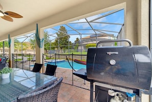 Eine Außenpatio mit einem Glastisch, Korbstühlen, einem Grill und einem Swimmingpool im Hintergrund.