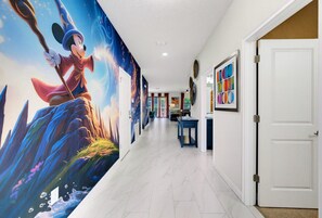 Un passadís amb un mural gran d'un personatge, una porta blanca i una taula amb objectes a sobre.