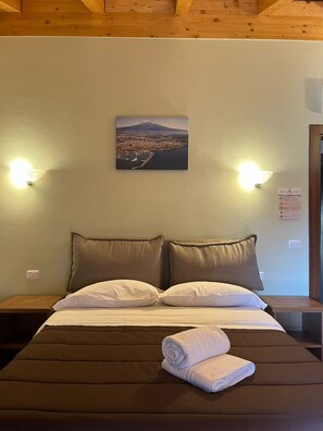 A hotel room with a bed, two pillows, a folded towel, and a wall-mounted picture.