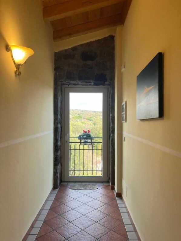 A hallway with a stone wall, a door leading to a balcony, and a painting on the wall.