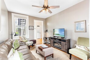 Een woonkamer met een plafondventilator, een televisie, een open haard en een bank.