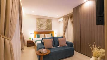 A modern bedroom with a bed, a blue sofa, a bedside table with books, and a wall-mounted air conditioner.