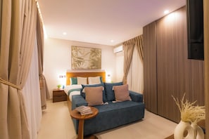 Ein modernes Schlafzimmer mit einem Bett, einem blauen Sofa, einem Nachttisch mit Büchern und einer Wand-Klimaanlage.
