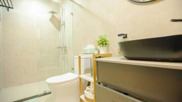 Un baño moderno con cabina de ducha de vidrio, un inodoro blanco y un tocador con lavamanos.