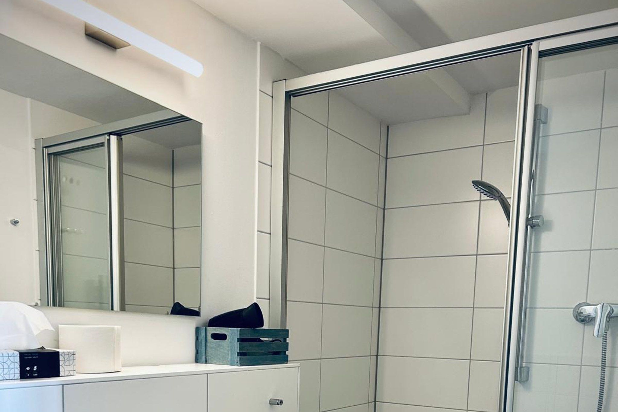 A modern bathroom with a glass shower enclosure, a white tiled wall, and a large mirror above a white vanity.