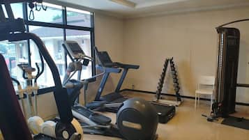 Ein Fitnessraum mit Trainingsgeräten, darunter Laufbänder, ein Crosstrainer und eine Gewichtbank.