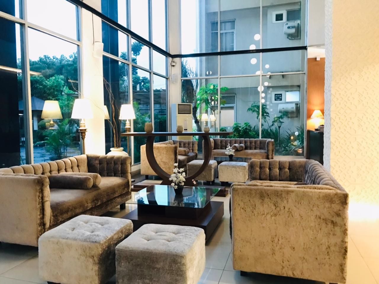 Eine geräumige Lobby im modernen Stil, mit einer Sitzecke mit Sofas und Poufs, einem zentralen Couchtisch und einem großen Fenster mit Blick ins Freie.