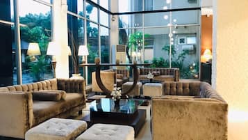 Eine geräumige Lobby im modernen Stil, mit einer Sitzecke mit Sofas und Poufs, einem zentralen Couchtisch und einem großen Fenster mit Blick ins Freie.