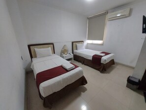 A hotel room with two beds, a bedside table with a lamp, and an air conditioning unit on the wall. - Geowisata Inn (Bandung)