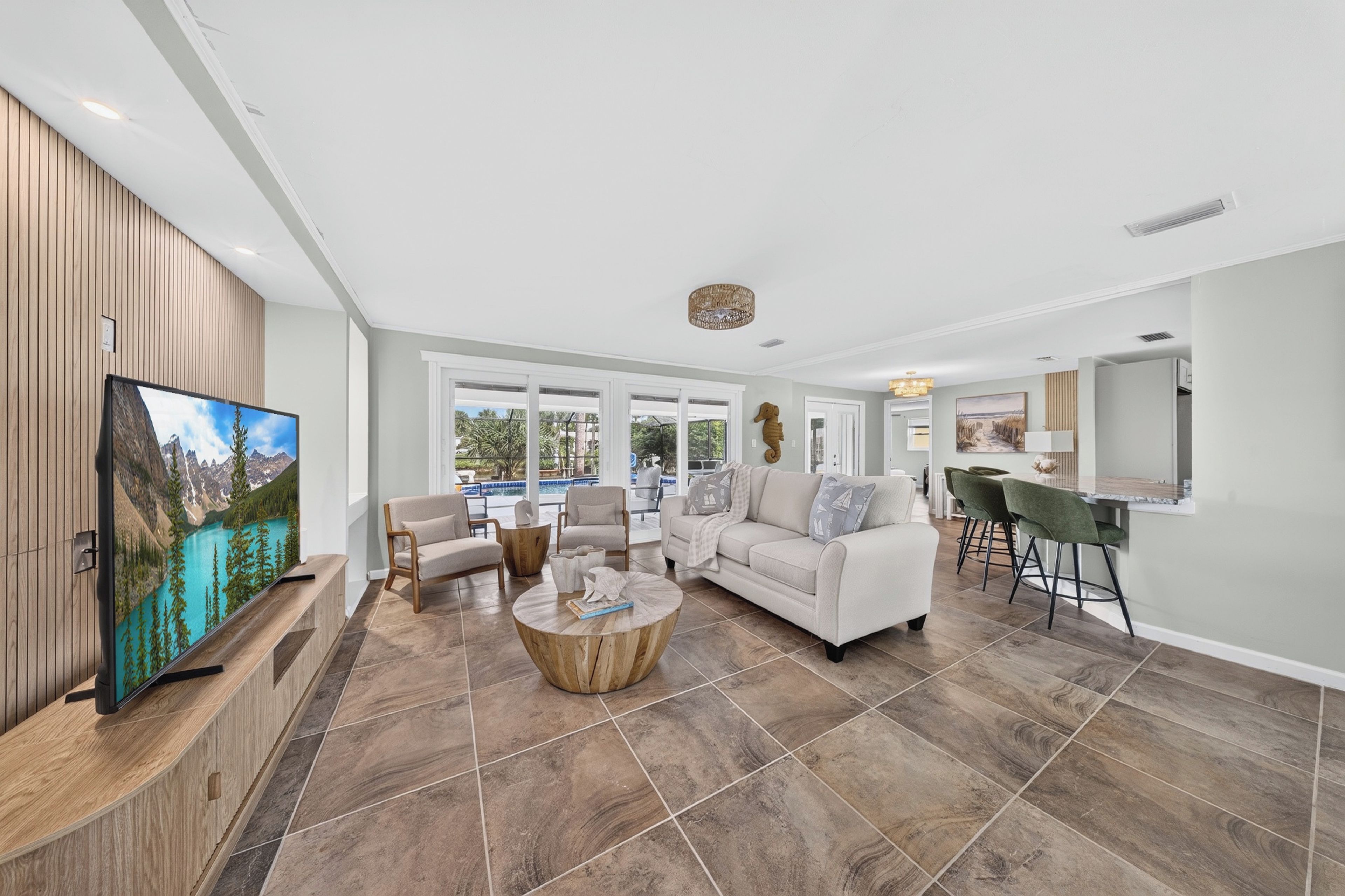 A spacious living area with a large flat-screen TV, a sofa, a coffee table, and a dining area with a bar.
