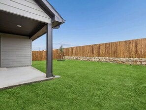 A residential property with a well-maintained lawn, a wooden fence, and a stone wall. - Modern 4BR Home • Office • Patio • 3 Full Baths (McKinney)