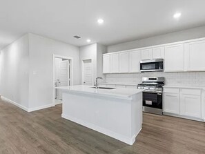 Une cuisine moderne avec des meubles blancs, un îlot central, un four à micro-ondes et une cuisinière.