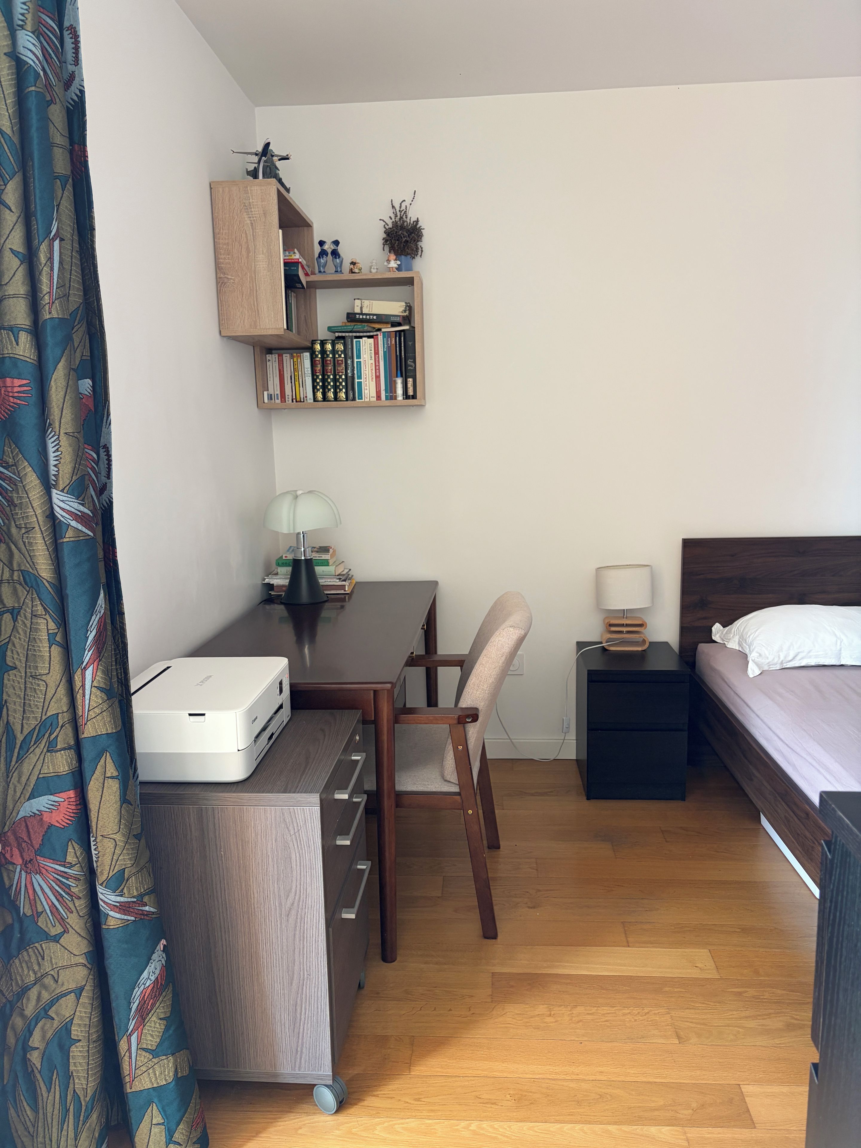 Une pièce de taille modeste comprenant un bureau, une chaise, un lit, une table de chevet et une bibliothèque.