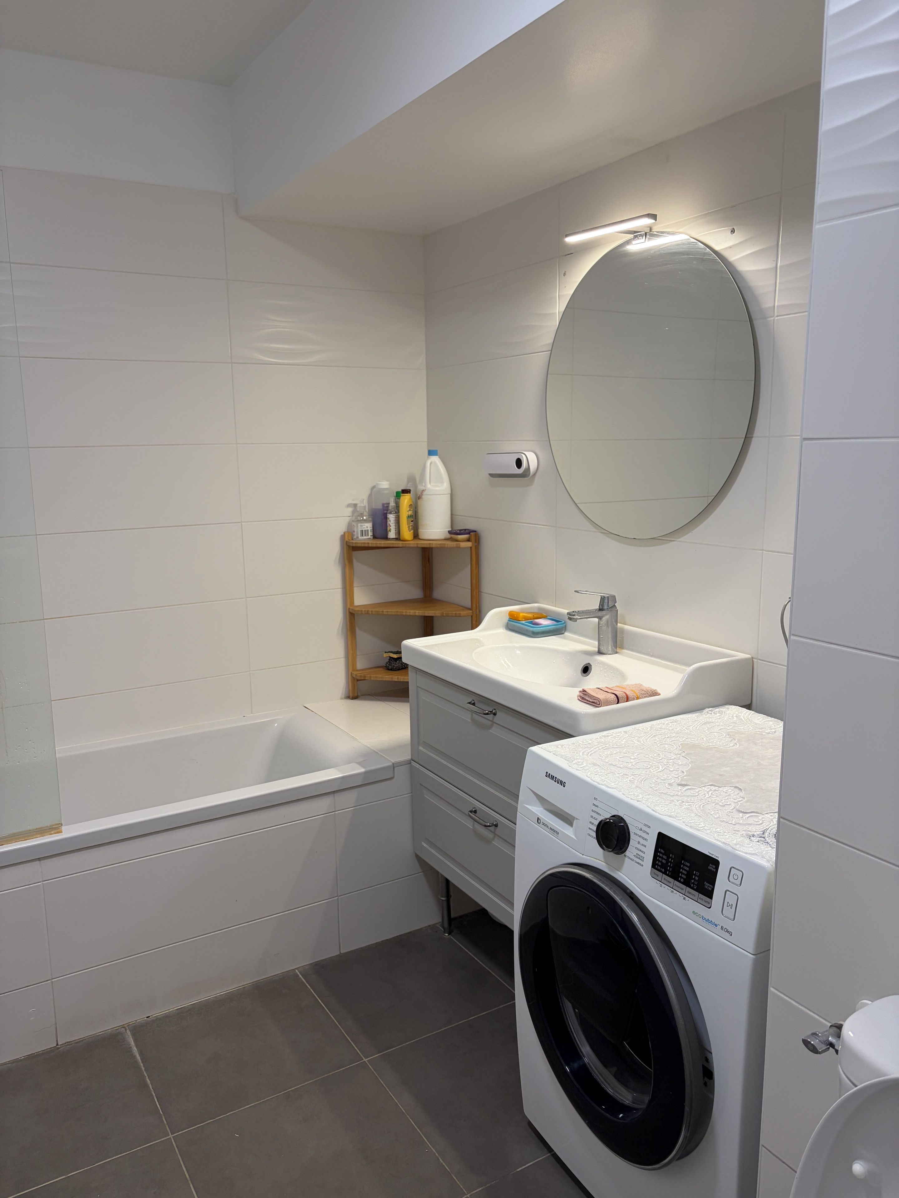 Een badkamer met een bad, een wasmachine, een wastafel met spiegel en een plank met toiletartikelen.