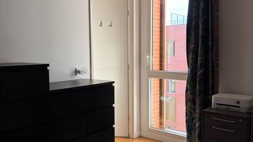 Een slaapkamer met een bed, een dressoir, een printer en een schuifpui naar een balkon.