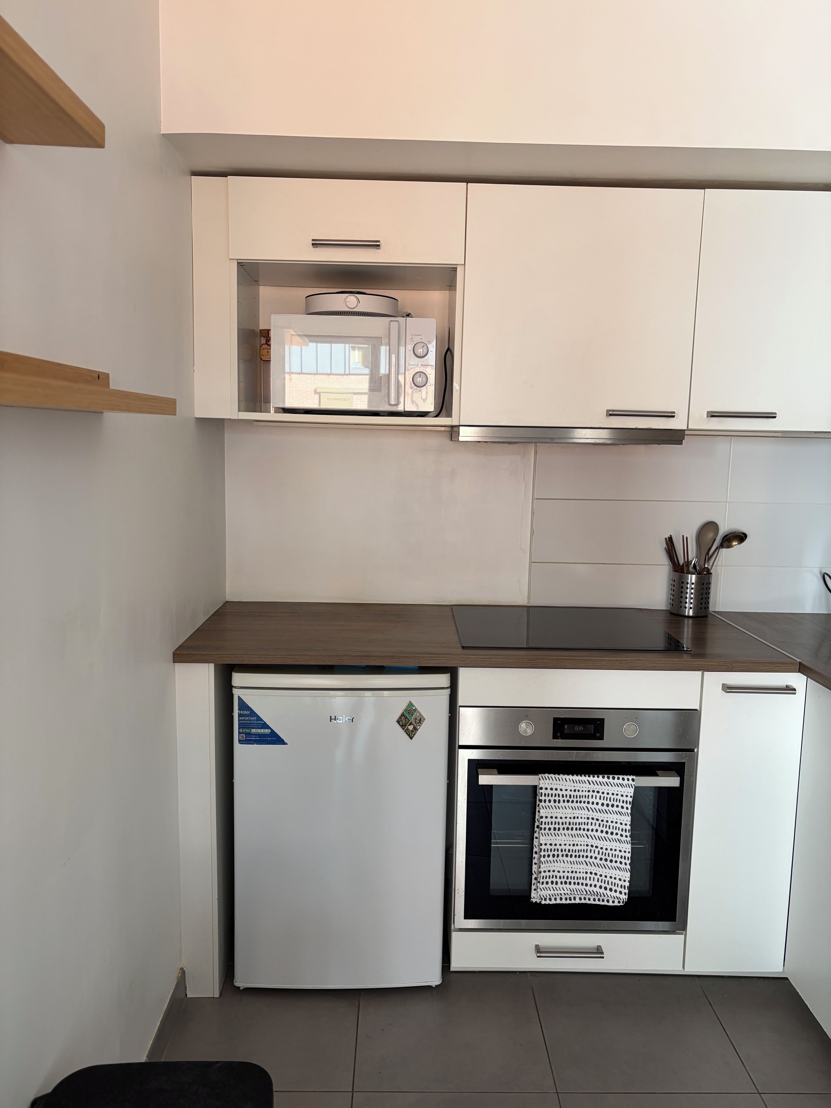 A compact kitchen with a built-in microwave, a small refrigerator, and an oven.