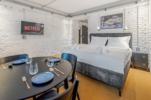 A hotel room with a bed, a dining table with chairs, a TV mounted on the wall, and a painting above the bed. - Studio with a private terrace | Karmelitermarkt (Wien)