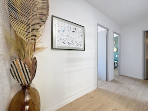 Ein Flur mit einem gerahmten Vogelbild an der Wand, einem gewobenen Korb und einer Vase mit einem gemusterten Deckel.