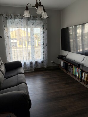 A living room with a sofa, a flat-screen TV, a bookshelf, and a window with curtains.